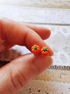 A pair of miniature pumpkin stud earrings held between finger and thumb