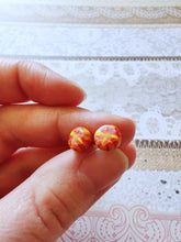 Load image into Gallery viewer, A pair of red and yellow stud earrings held between finger and thumb

