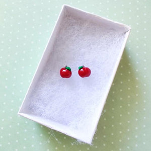 A pair of miniature apple earrings inside a white paper jewelry box