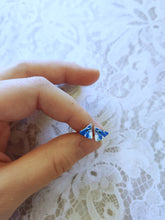 Load image into Gallery viewer, A pair of blue, white, and silver triangle earrings held between finger and thumb
