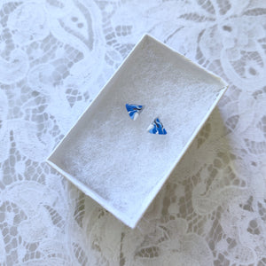 A pair of triangular blue white and silver earrings in a white paper jewelry box