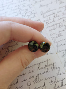 Yellow, black, and orange swirl earrings held between finger and thumb