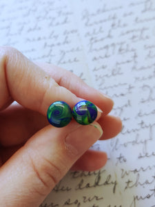 Yellow, blue, and purple swirl earrings held between finger and thumb