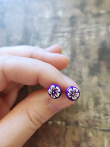 White and gold flowers on a purple background stud earrings held between finger and thumb