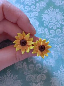 Two 3/4 inch sunflower earring studs held between finger and thumb