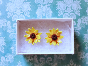 Two sunflower earrings in a white paper jewelry box