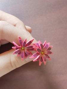Pink and purple aster flower shaped stud earrings held between finger and thumb