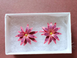Pink and purple aster flower shaped stud earrings in a white paper jewelry box