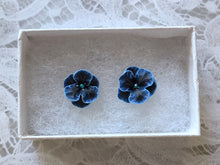 Load image into Gallery viewer, Blue and black flower shaped earrings with blue metallic centers inside a white paper jewelry box.

