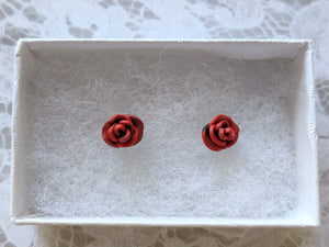 A pair of red and black rose flower earrings inside a white paper jewelry box.