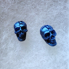 Load image into Gallery viewer, A close of picture of metallic  sapphire colored skull earrings attached to plastic posts. 
