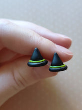 Load image into Gallery viewer, A pair of black witches hats with yellow bands made into flat backed stud earrings. Earrings are displayed between finger and thumb.
