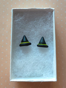 A pair of black witches hats with yellow bands made into flat backed stud earrings. Earrings are displayed in a white paper jewelry box. 