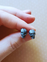 Load image into Gallery viewer, Grey colored skull stud earrings that shimmer silvery in the light. 
