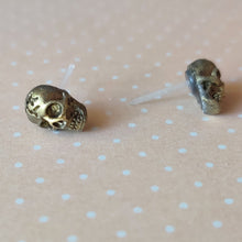 Load image into Gallery viewer, Faux aged gold skull earrings attached to plastic posts displayed on a pale orange background with white polka dots.
