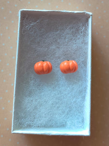 A pair of flat backed, side view, orange pumpkin earrings inside a white paper jewelry box.