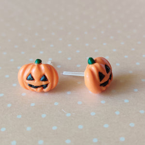 A pair of flat backed jack o' lantern earrings with relief sculpted detail and painted on face and stem. The earrings are sitting on a orange and white polka dot background. 