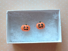 Load image into Gallery viewer, A pair of flat backed jack o&#39; lantern earrings with relief sculpted detail and painted on face and stem. The earrings are inside a white paper jewelry box.
