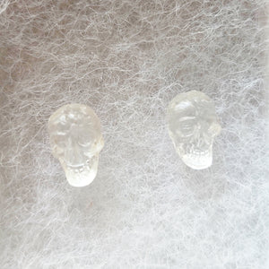 A close up picture of a pair of clear skull stud earrings. 