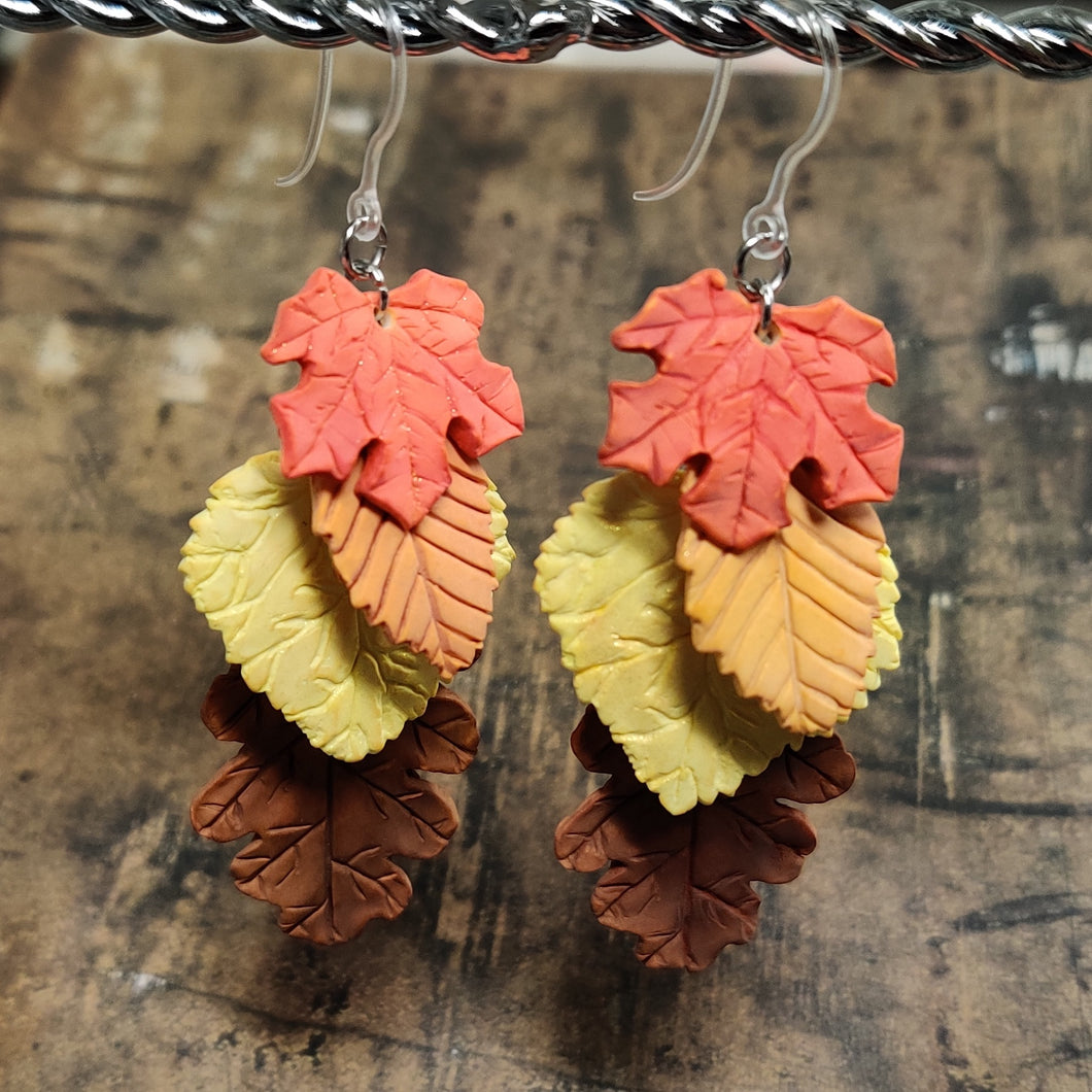 Two dangle earrings with fall leaves cascading down as if stacked on top of each other. A red maple leaf is on top, followed by an orange beech, and yellow aspen, and a brown oak.