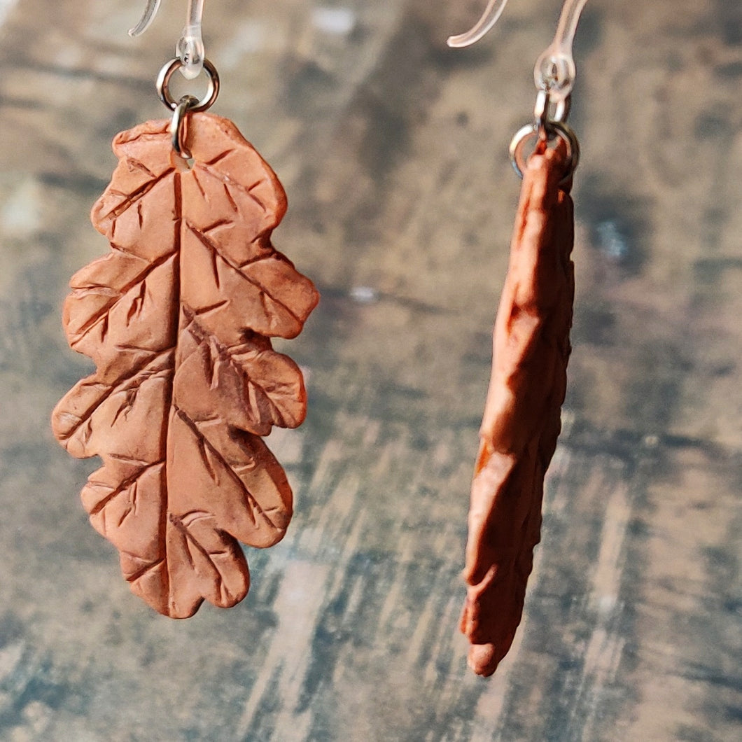 Close up image of a pair of rust brown oak leaf shaped polymer clay earrings on plastic ear hooks