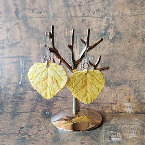 A pair of yellow Aspen leaf shaped polymer clay earrings are displayed hanging from a small, polished silver tree shaped display.