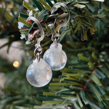 Load image into Gallery viewer, Two miniature Christmas ornament baubles in a clear color with silvery white swirls inside. The earrings are shown hanging from the branch of an artificial Christmas tree. 
