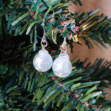 Load image into Gallery viewer, Two miniature Christmas ornament baubles in a clear color with silvery white swirls inside. The earrings are shown hanging from the branch of an artificial Christmas tree. 
