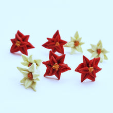 Load image into Gallery viewer, Two pairs each of white and red Poinsettia earrings displayed on white paper. One pair of each color is in focus in the foreground, and one of each color is out of focus in the background. 
