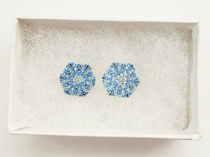 Two hexagon shaped earrings with intricate white, silver and blue patterns inside a white paper jewelry box.