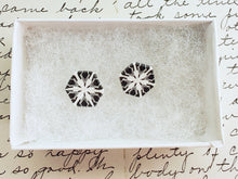 Load image into Gallery viewer, Two hexagon shaped earrings with a snowflake pattern in silver and white. They are in a white paper jewelry box. 
