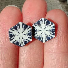 Load image into Gallery viewer, Two hexagon shaped earrings with a snowflake pattern in silver and white. The earrings are held in bright sunlight and have small silver sparkles in the grey areas. 
