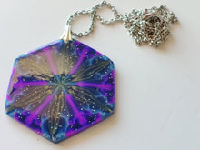 Load image into Gallery viewer, A large hexagonal pendant  connected to a silver colored chain and bail. The pendent is dark blue with purple, gold, and light blue colors radiating out from the center. It is displayed laying on a white plain ceramic tile.
