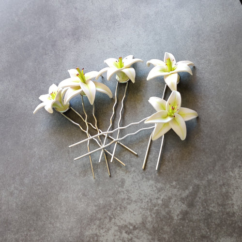 A set of five medium sized white lily hair pins on a mottled grey background.
