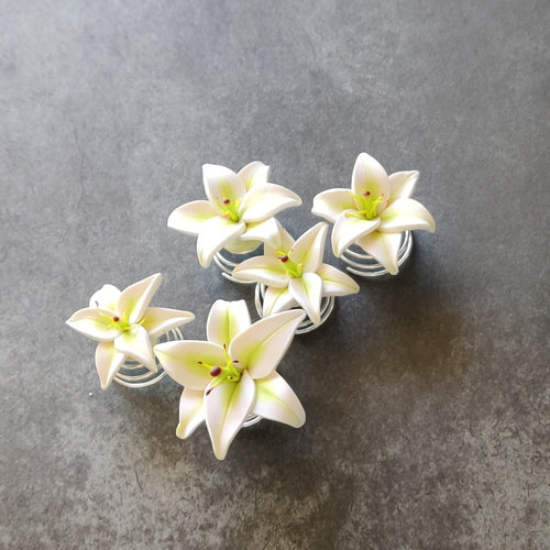 A set of five white lily spin pins. The wire spirals out from the bottom of the flower in a short cone shape. 