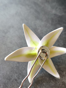 An image showing the back of the white lily hair pin. The silver colored bezel and hair pin are visible with the white petals and green veins showing from the back of the flower.