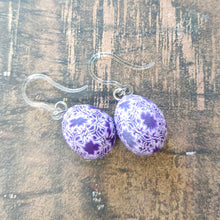 Load image into Gallery viewer, Patterned Easter egg shaped dangle earrings in a purple and white one a brown paper background.
