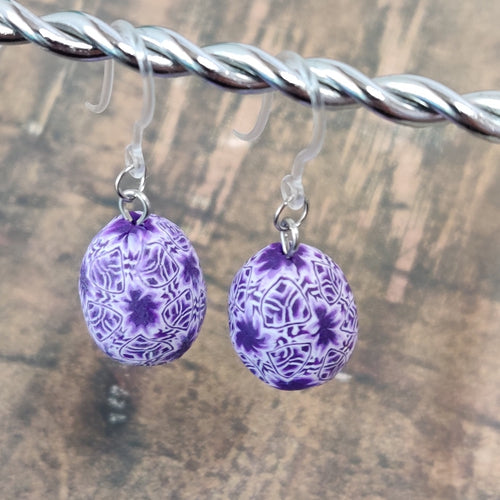 Patterned Easter egg shaped dangle earrings in a purple and white color hanging from a silver wire. 